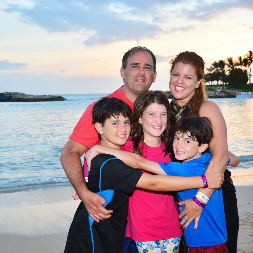 Patty and husband arms wrapping around three children and the beach in the background